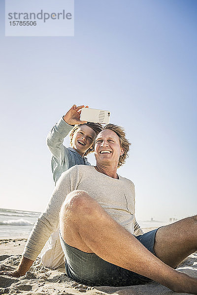 Vater amüsiert sich mit seinem Sohn am Strand und macht Smartphone-Fotos