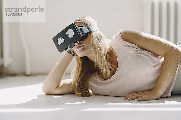 Auf dem Boden liegende junge Frau mit VR-Brille und schielenden Augen