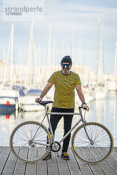 Porträt eines lächelnden  reifen Mannes  der mit einem Fixie-Rad auf einer Strandpromenade steht  Alicante  Spanien