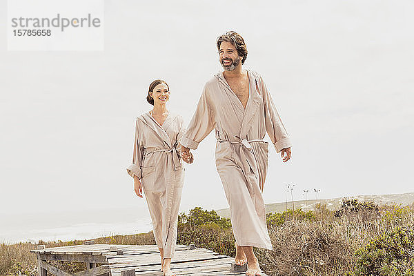 Glückliches Paar in Bademänteln beim Spaziergang auf der Strandpromenade an der Küste