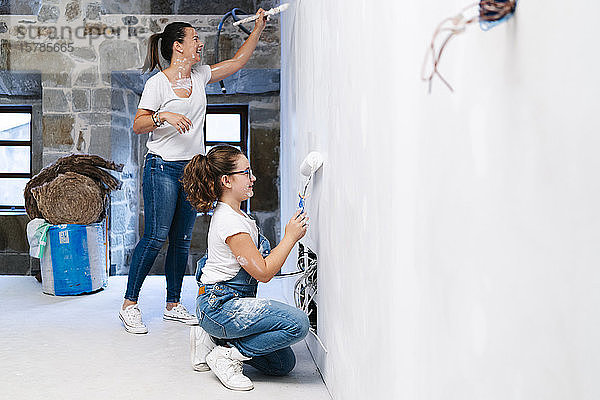 Mutter und Tochter streichen gemeinsam eine Wand ihres neuen Hauses