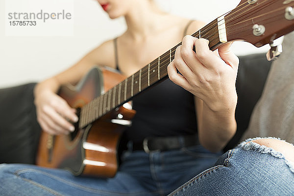 Schrägansicht einer jungen Frau  die auf einer Couch sitzt und Gitarre spielt