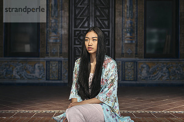 Porträt einer schönen jungen Frau  die auf einer Treppe sitzt und einen Kimono trägt