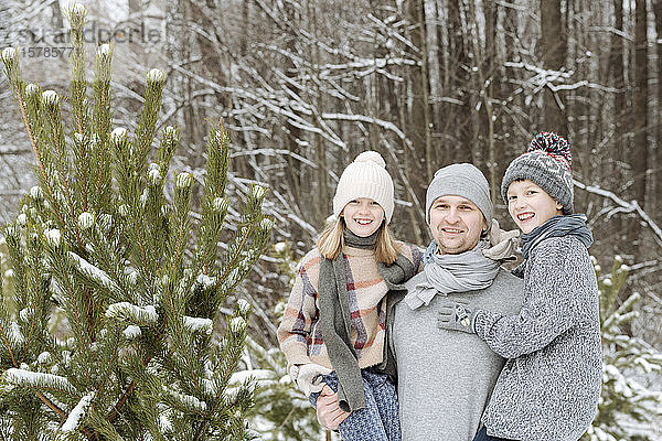 Porträt eines glücklichen Vaters mit zwei Kindern an einer Tanne im Winter