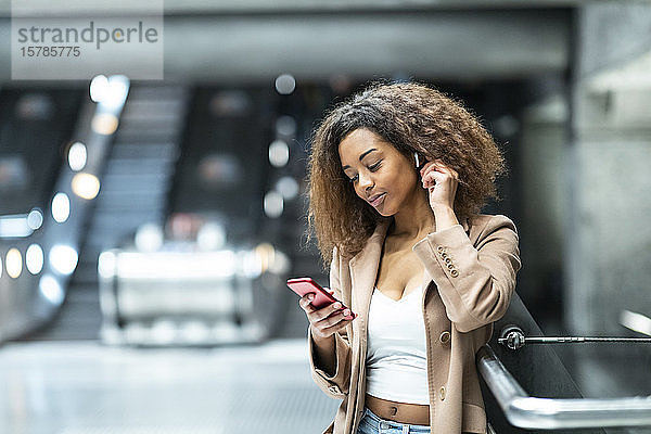 Junge Frau mit Handy und Ohrstöpseln in der U-Bahn-Station