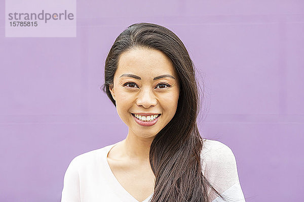 Bildnis einer glücklichen Frau mit langen braunen Haaren vor violettem Hintergrund