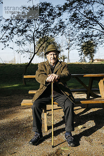 Alter Mann mit Stock auf einer Bank in einem Park sitzend
