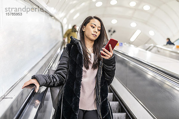 Porträt einer Frau  die auf der Rolltreppe steht und auf ein Handy schaut  London  UK
