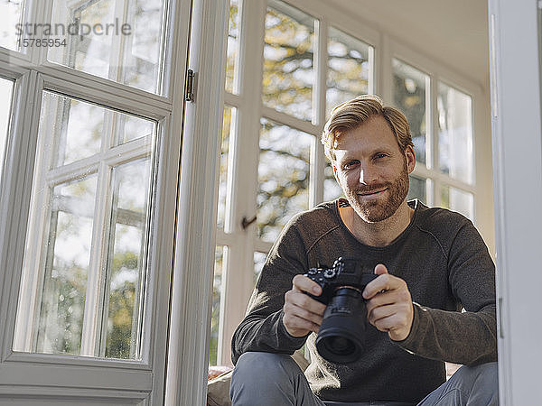 Porträt eines Mannes mit Kamera im Sonnenzimmer zu Hause