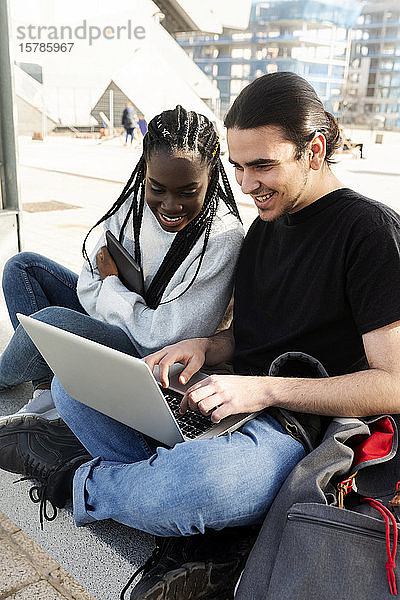 Glückliches junges Paar mit Laptop an der Straßenbahnhaltestelle