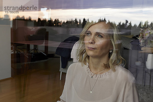 Porträt einer blonden Frau hinter einer Fensterscheibe zu Hause