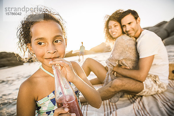 Mädchen mit ihrer Familie bei Sonnenuntergang am Strand bei einem Erfrischungsgetränk