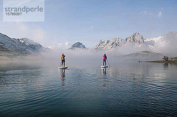 Zwei Frauen stehen beim Paddel-Surfen auf einem See auf