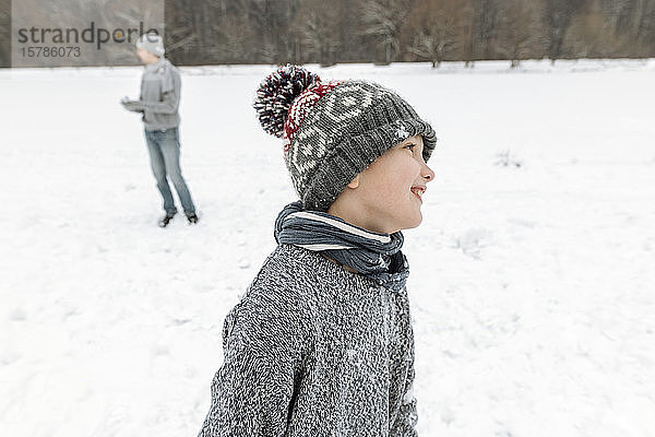 Porträt eines lächelnden Jungen in Winterlandschaft mit Vater im Hintergrund