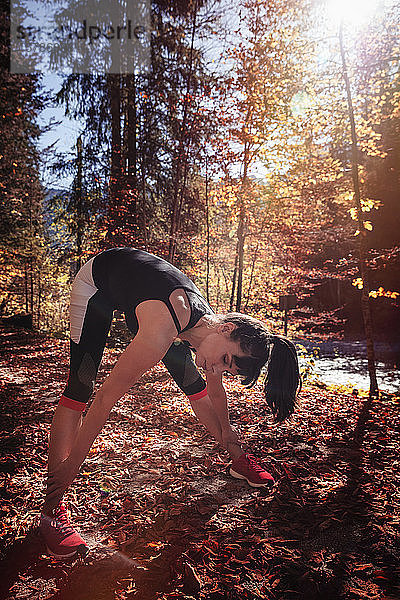 Frau joggt im Herbstwald  streckt sich zum Aufwärmen