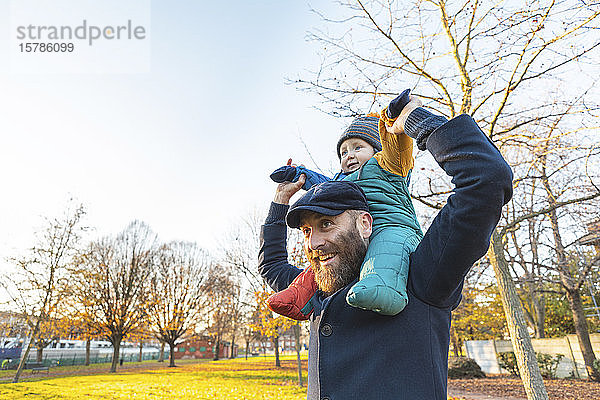 Glücklicher Mann trägt seinen kleinen Sohn im Park auf den Schultern