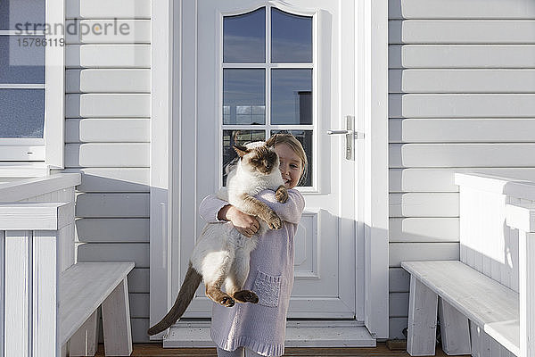 Kleines Mädchen mit Katze auf dem Arm vor dem Hauseingang
