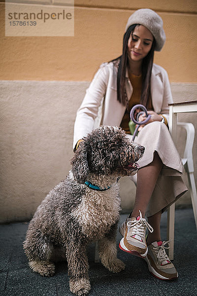 Junge Frau sitzt mit ihrem Hund in einem Café in der Stadt