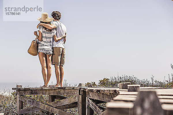 Junges Paar  das auf einer Strandpromenade an der Küste steht und die Aussicht betrachtet
