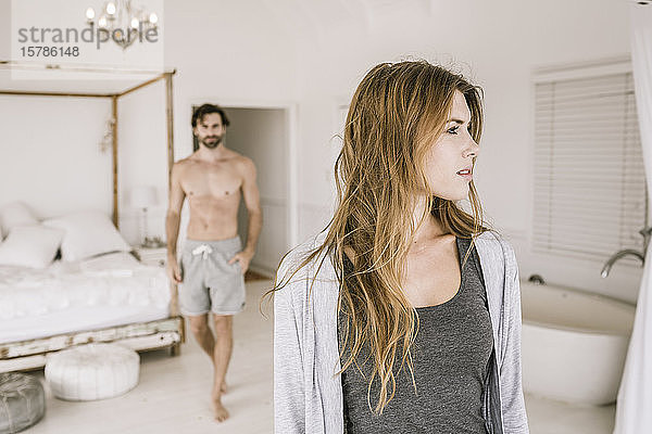 Porträt einer seriösen jungen Frau im Schlafzimmer mit Mann im Hintergrund