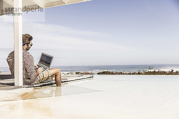 Mann arbeitet am Laptop neben dem Pool in einem Strandhaus