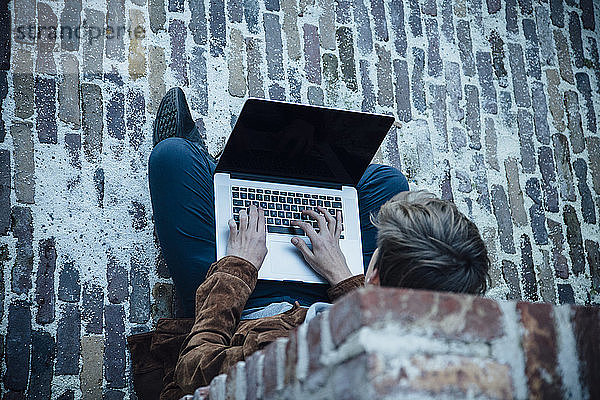 Teenager  der einen Laptop benutzt und auf einem Steinboden in der Stadt sitzt