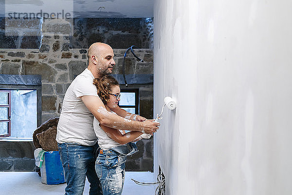 Vater und Tochter streichen gemeinsam eine Wand ihres neuen Hauses