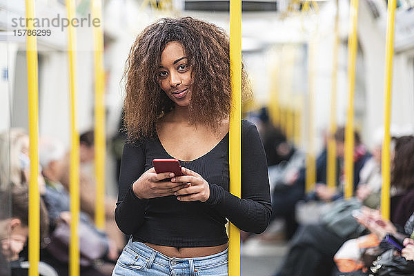 Porträt einer lächelnden jungen Frau mit Smartphone in der U-Bahn
