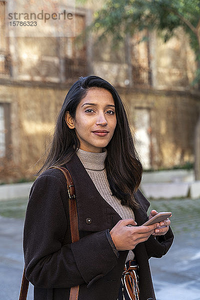 Porträt einer selbstbewussten jungen Frau mit Smartphone in der Stadt