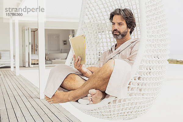 Entspannter Mann im Bademantel beim Lesen eines Buches im Hängesessel