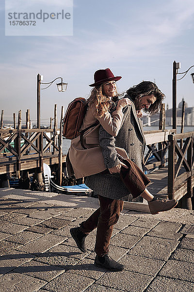 Junger Mann nimmt seine Freundin am Hafen von Venedig  Italien  huckepack