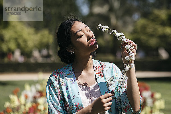 Schöne junge Frau hält im Frühling eine Blume in einem öffentlichen Garten