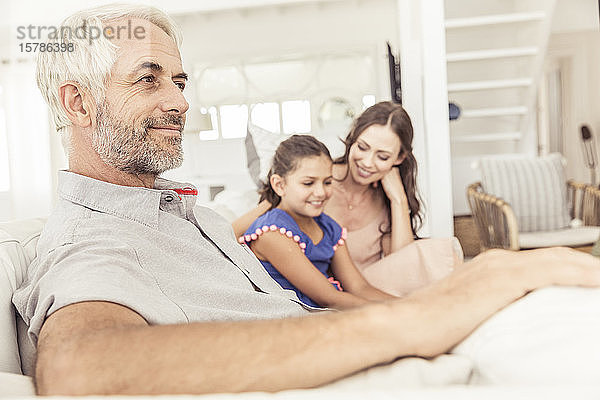 Lächelnder reifer Mann mit Familie auf der Couch im Wohnzimmer