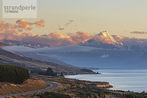 Neuseeland  Blick auf den neuseeländischen State Highway 80  der sich in der Morgendämmerung entlang des Ufers des Pukaki-Sees erstreckt  mit Mount Cook im Hintergrund