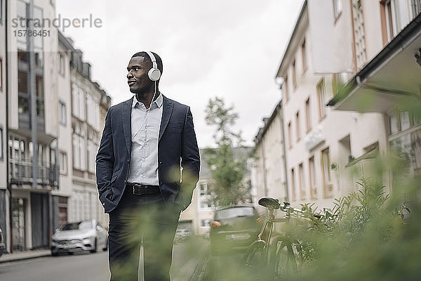 Junger Geschäftsmann  der auf der Straße mit Kopfhörern Musik hört