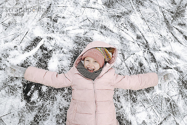 Porträt eines glücklichen Mädchens mit ausgestreckten Armen auf Eis liegend