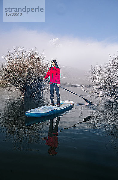 Frau steht beim Paddel-Surfen auf einem See auf
