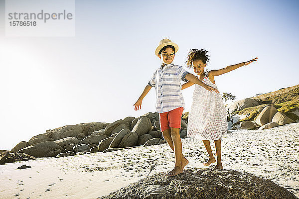 Glückliche Jungen und Mädchen balancieren auf einem Felsen am Strand