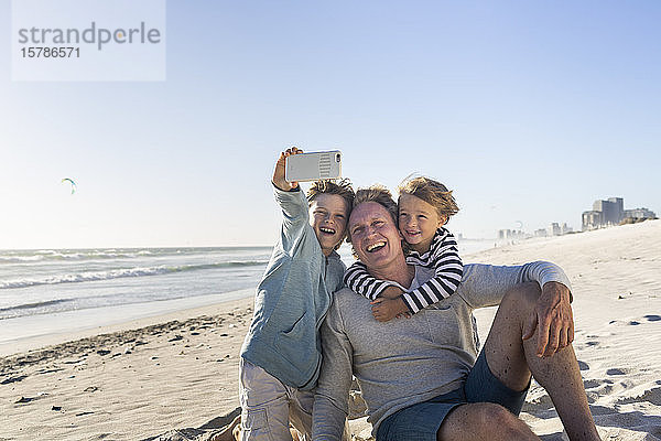 Vater amüsiert sich mit seinen Söhnen am Strand und macht Smartphone-Fotos