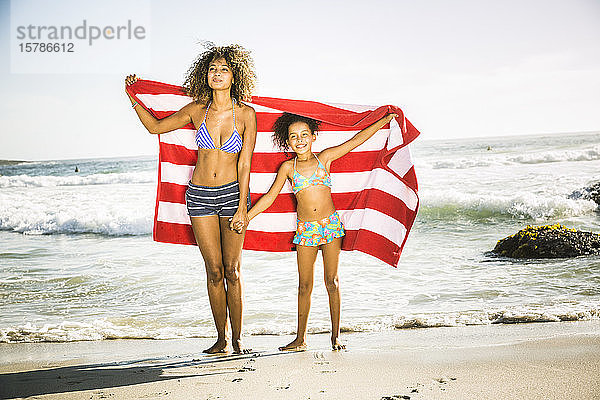 Glückliche Mutter und Tochter mit Handtuch am Strand stehend