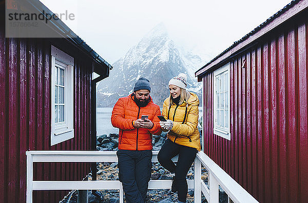Touristenpaar mit Smartphones auf einer Veranda auf Hamnoy  Lofoten  Norwegen