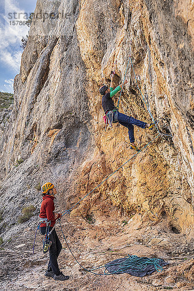 Frau sichert Mann beim Klettern an Felswand