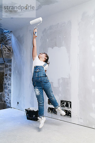Mädchen  das springt  während es eine Wand in einem Haus streicht