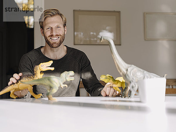 Porträt eines lächelnden Mannes mit Spielzeugdinosauriern auf dem Tisch