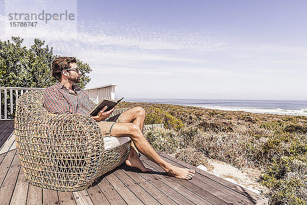 Mann liest ein Buch auf einem Deck an der Küste