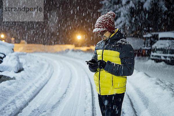 Mann benutzt Mobiltelefon bei Schneefall in der Nacht
