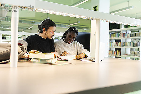 Zwei Studenten mit Laptop und Büchern lernen in einer Bibliothek