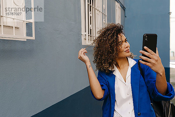 Porträt einer lächelnden Frau  die mit ihrem Smartphone einen Selfie macht