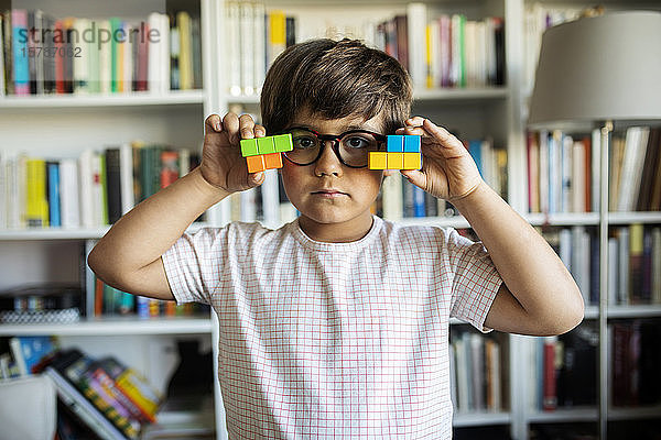 Porträt eines ernsten kleinen Jungen mit Brille  der zu Hause mit Bauklötzen spielt