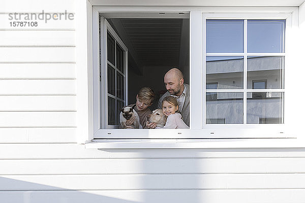 Vater mit seinen zwei Kindern  Hund und Katze am geöffneten Fenster ihres Hauses